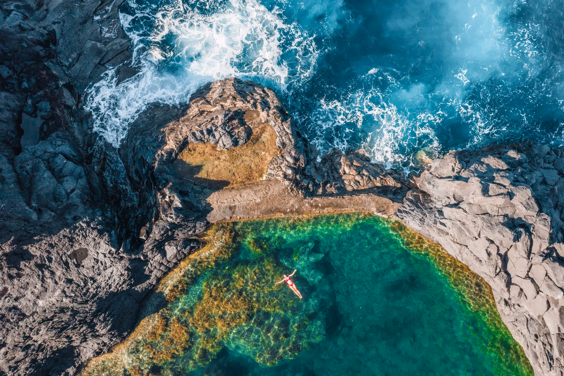 Aerial view of a swimmer in a natural rock pool on Madeira's coast
