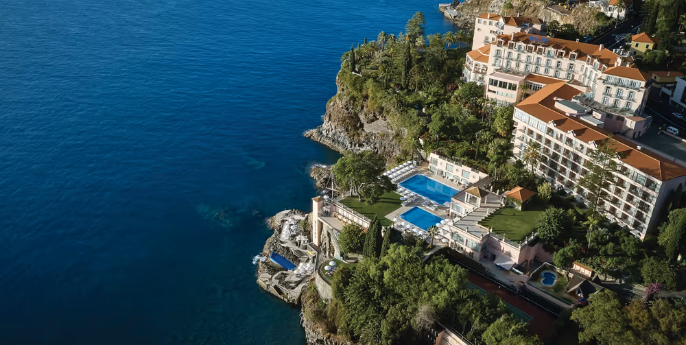 Clifftop pool terrace framed by palms at Belmond Reid's Palace above Funchal bay, Madeira